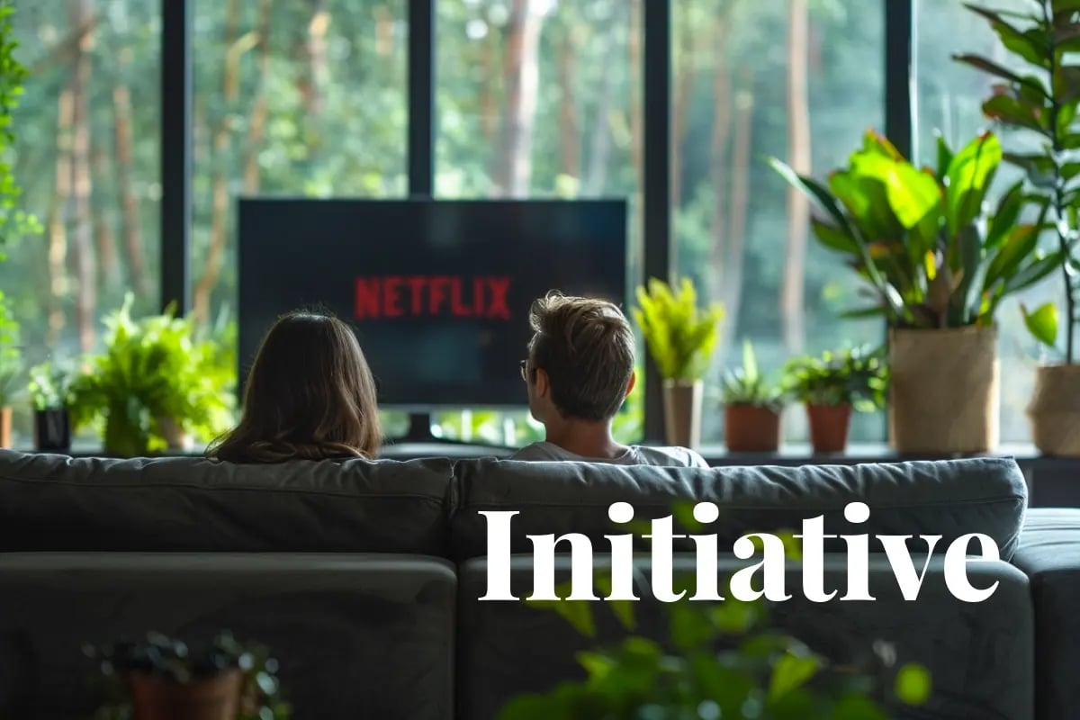 Netflix backs 15-year carbon credit deal to expand US reforestation_Two people watching TV in their apartment with a green forest outside the window_visual 1