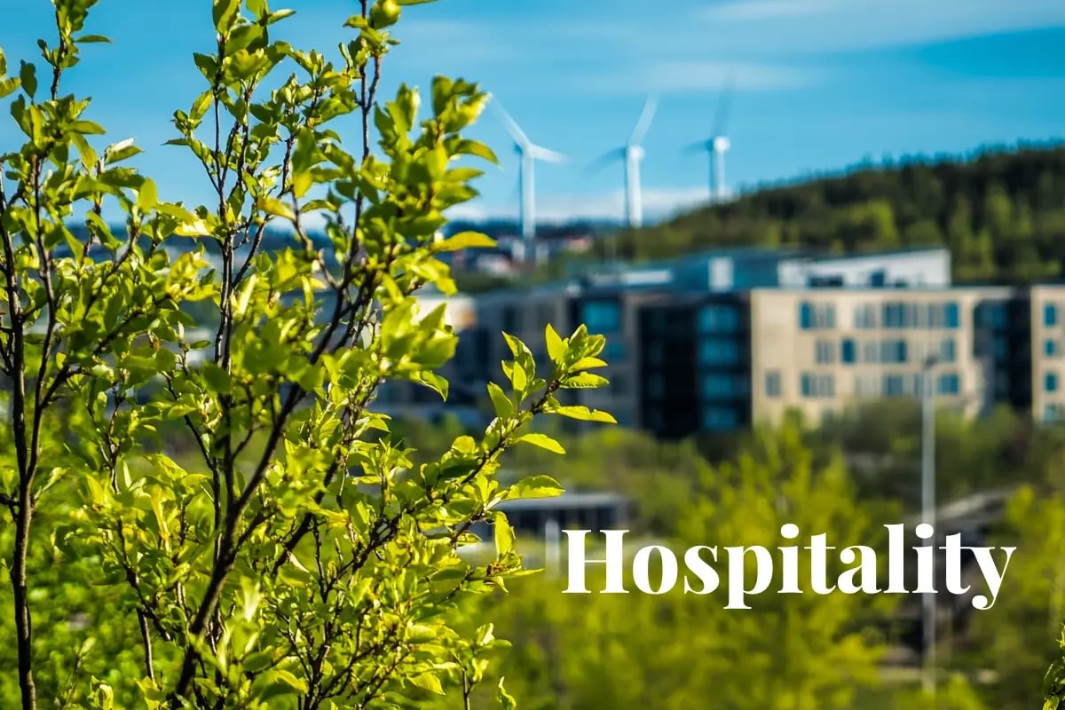 Radisson sets the bar with first verified net-zero hotels in Europe_Foreground of young green trees with a modern Radisson hotel and distant wind turbines under a clear blue sky in Oslo_visual 1